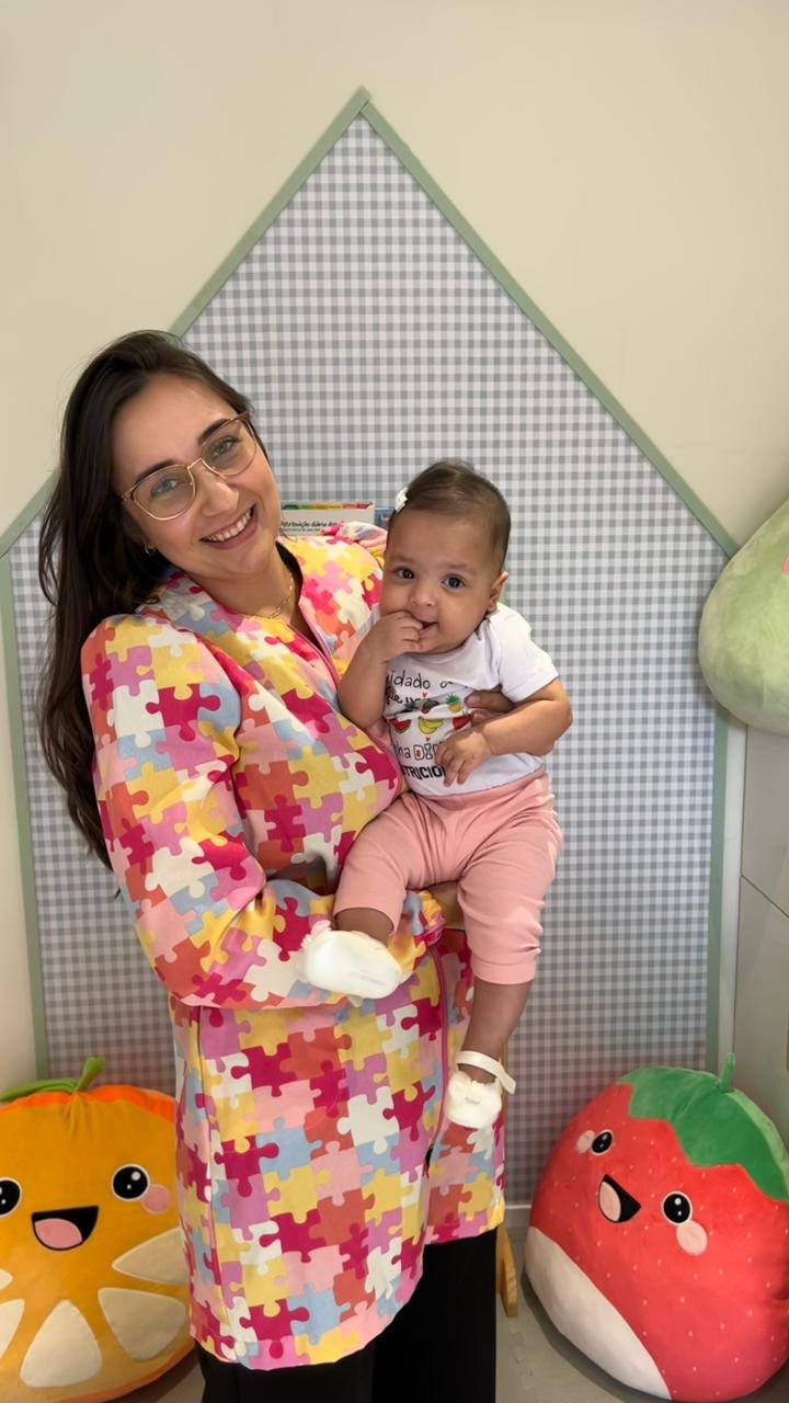 Nutricionista infantil Gaby Roncaglio sorrindo e segurando um bebê no colo em seu consultório lúdico de nutrição materno-infantil.
