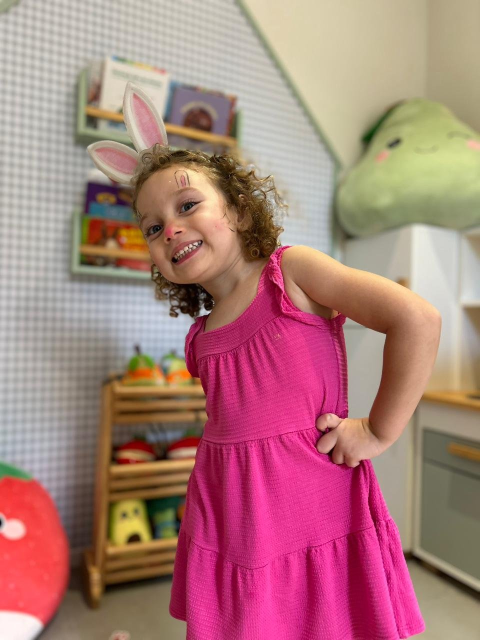 Menina sorridente usando tiara de orelhas de coelho e maquiagem artística fazendo pose durante a oficina culinária infantil de Páscoa.